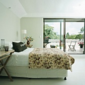Doppelbett und geblümte Tagesdecke vor Schiebefenster mit Blick auf den Balkon