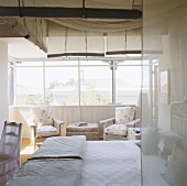Schlafzimmer mit Himmelbett vor einer Fensterfront und zwei Polstersesseln