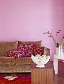 Braunes Stoffsofa mit pinken Zierkissen und Damenhausschuhe vor rosa Wand