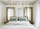 Samtkissen auf einem Doppelbett mit Kopfteil aus Ästen, dahinter zwei barocke Spiegel