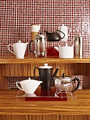 Verschiedene Kaffee- und Teekannen auf Holzunterlage vor rote Mosaikfliesenwand