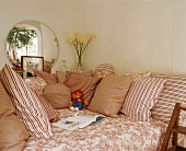 Patterns of white and red on comfortable sofa with many scatter cushions below round mirror on wall