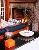 Offener Kamin mit loderndem Feuer hinter einer mit schwarzerm Leder bezogenen Wohnzimmercouch