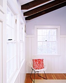 Weisser Metallstuhl mit rot-weißem Zierkissen in einer Ecke stehend