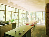 Offener Wohnraum mit großer Fensterfront, moderner Küche und einem langen Esstisch im Essbereich