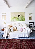Couch mit großzügigem Überwurf und vielen Kissen; darüber ein modernes Gemälde