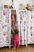 Kleines Mädchen schiebt den Vorhang ihres Kleiderschranks beiseite