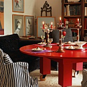 Wohnraumecke mit einem runden, massiven Holztisch in Rot mit Rollen und Kerzendekoration