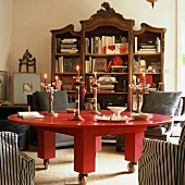 Runder, massiver Tisch in Rot mit Rollen vor antikem Bücherschrank mit vielen Büchern