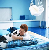 Frau liegt mit Katze auf Matratze in blauem Schlafraum