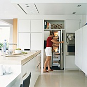 Frau steht am geöffneten Kühlschrank in der Küche