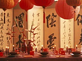 Asiatisch gedeckter Tisch mit Lampions, Kerzen & Paravent im Hintergrund