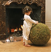 Kleines Mädchen in Engelsflügeln spielt vor dem Kamin