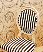 Barocker Stuhl mit gestreifter Polsterung vor romantischer Tapete mit Puttenmotiv