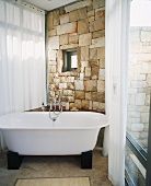 Freistehende Badewanne in einem Badezimmer mit raumhohen Fenstern und Natursteinwand