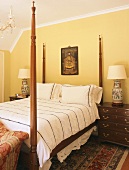 Doppelbett mit gotischen Ecksäulen aus Holz in einem Raum mit halbschräger Decke und Deckenleiste