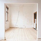 Blick in ein leerstehendes, renovierungsbedürftiges Zimmer mit Dielenboden