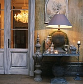 Der antike Wandtisch mit großer Tischleuchte und Dekoartikeln aus Glas neben einer alten Salontür bilden ein effektvolles Arrangement