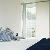 Gestreifte Kissen auf einem Bett mit Blick ins Grüne durch die raumhohen Fenster