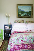 Ein lebhaftes Schlafzimmer im Stilmix mit bunt gemusterter Bettwäsche, barockem Landschaftsgemälde und antikem Beistelltisch