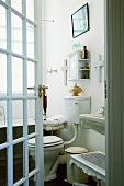 Blick durch die halb geöffnete Sprossentür in ein weisses Badezimmer mit Vintageelementen