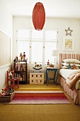 Ein verspielt-romantisches Kinderzimmer mit senfgelbem Sisalboden und buntem Streifenteppich
