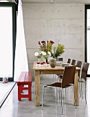 Moderne Stühle une eine rote Holzbank an einem einfachen, antiken Esstisch mit Blumenvasen und Geschirr