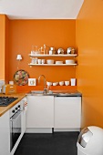 Leuchtendes Orange an der Wand wertet die schlichte weiße Küchenzeile auf