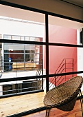 Ein Schalenstuhl aus Korbgeflecht vor einer verglasten Wand mit Blick ins helle Treppenhaus