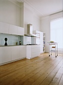 Eine moderne Küchenzeile mit weissen Schrankfronten im Altbau mit Dielenboden, Stuckdecke und großem, raumhohem Fenster