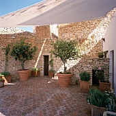 Ein reich begrünter Innenhof im Rustico Stil mit schattenspendendem Sonnensegel