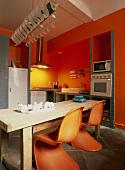 Zwei Panton Stühle an einem rustikalen Holztisch bilden den Höhepunkt der individuellen Küche mit roten Wänden und Stauraumnischen