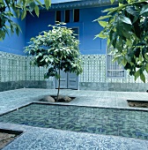 Ornamentik in Blau und Grün dominiert den orientalischen Innenhof mit kleinem Wasserbecken und jungen Bäumen