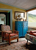 Blaue Vintagekommode und alter Kirschholzsessel im Wohnzimmer mit schräger Holzdecke
