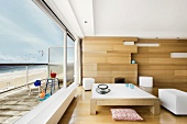 Couchtisch vor Holzpaneelwand im modernen Wohnzimmer mit Panoramablick auf den Strand