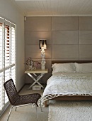 Netzartige Tagesdecke auf dem Bett und moderner Beistelltisch mit Chromklappfüßen vor gepolstertem Wandpaneel