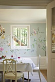 Blick auf einen gedeckten Esstisch vor einer Wand mit Sprossenfenster und floraler Wandmalerei