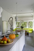 Marmorküchentheke mit Spülbrause und Obstschale vor einer hellen Essecke am Fenster mit grünen Sitzpolstern