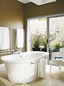 Moderne, freistehende Badewanne in einem braun gestrichenen Badezimmer mit Terrassenzugang