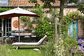 Sonnenschirm und Liegestuhl im idyllischen Garten eines Wohnhauses mit Backsteinfassade
