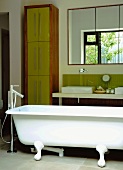 Freistehende Antikwanne mit moderner Armatur vor minimalistischen Waschtisch und hohem Badezimmerschrank