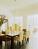 Gelb dekorierter Esstisch in einem hellen, klassischen Esszimmer mit Sprossentür zur Terrasse