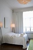 Schlafzimmer mit weißem Doppelbett, weißem Bild und zwei filigranen Stehlampen mit Stofflampenschirmen