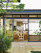 Blick von der gefliesten Gartenterrasse in den Wohn- und Essraum mit großer Glasfront