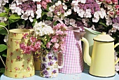 Jugs and pots in front of flowering shrub out of doors