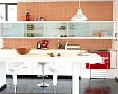 Rot-weiße Küche im Fiftiesstil mit langestreckter Küchenzeile, Hängeschränken, karierter Tapete, Bar & Hockern