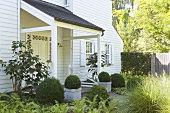 Weisses Holzhaus mit überdachtem Eingangsbereich, Grünpflanzen & Buchsbäumen