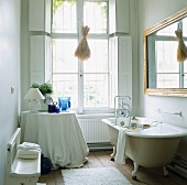 Weisses Badezimmer in Altbau mit Fenster, freistehender Badewanne, Wandspiegel & rundem Ablagetisch