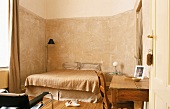 Schlafraum in Naturtönen mit hohen Wänden, Doppelbett & altem Holztisch