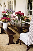 Holztischgarnitur auf Veranda mit zahlreichen Blumensträussen in Vasen & Eimern